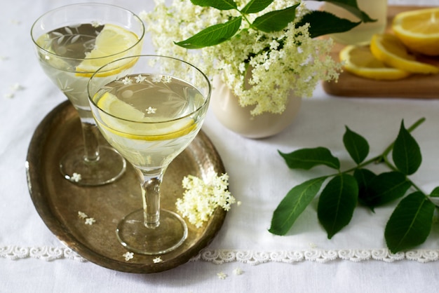 Una bevanda fresca con sciroppo di limone e fiori di sambuco in bicchieri su un vassoio di metallo. stile rustico.