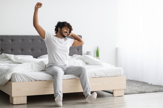 Cool eastern millennial guy stretching in bed