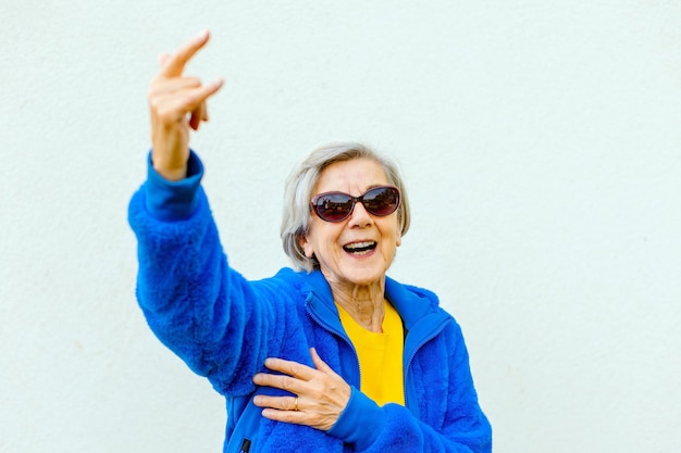 Cool elder woman forever young wearing sun glasses making rock sign