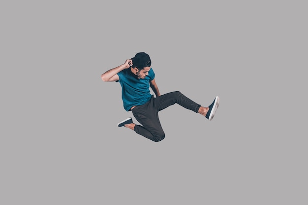 Cool and free. Mid-air shot of handsome young man in cap jumping and gesturing against background