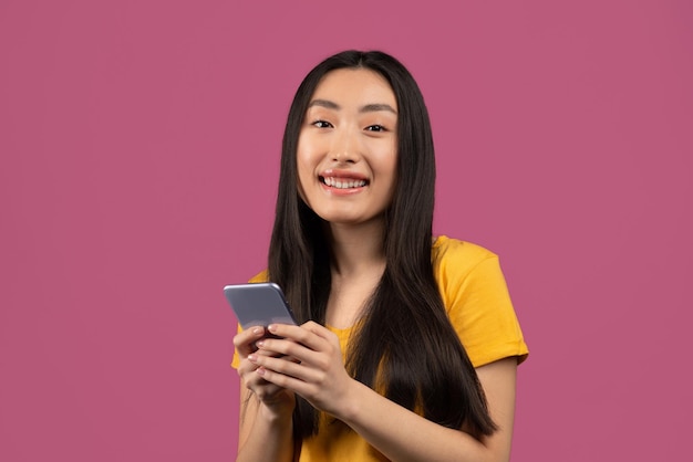 Cool gadget and app happy korean lady using smartphone and
smiling at camera standing on violet