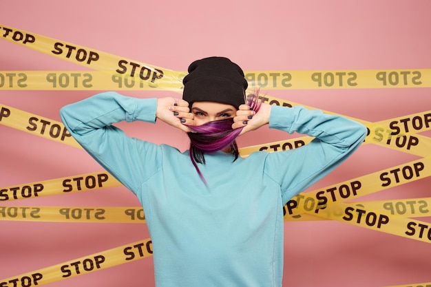 Cool girl with purple hair stands on the background of pink wall with the yellow tapes stop