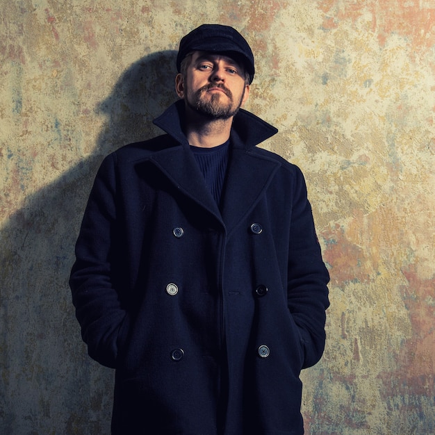 Cool guy rocks coat  and newsboy cap as he takes a moment to think