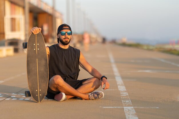 A cool guy sitting on a road with his skateboard