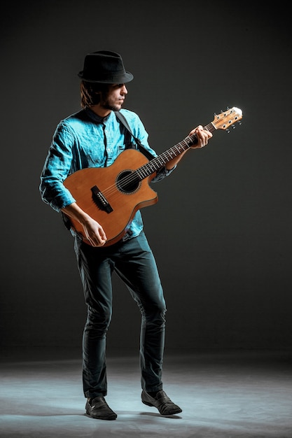 Cool guy standing with guitar on dark background