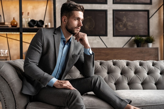 Cool and handsome. Good looking young man in full suit sitting on the sofa while spending time indoors.