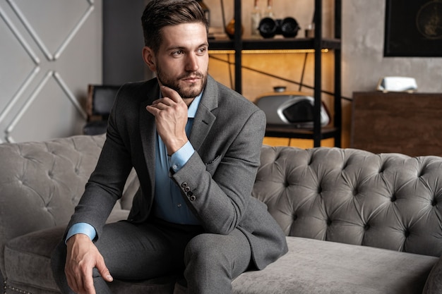 Cool and handsome. Good looking young man in full suit sitting on the sofa while spending time indoors.