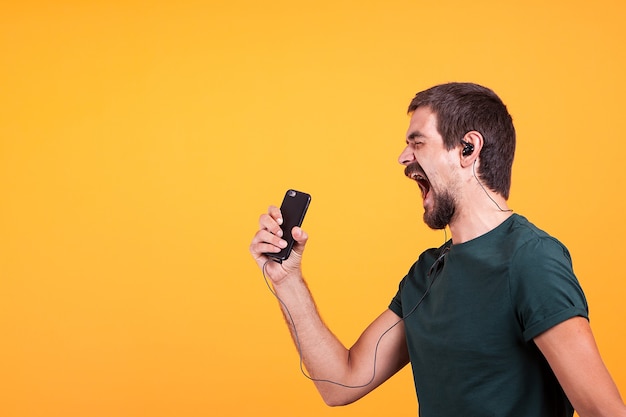 Cool joyful young man listening and enjoying music in his headphones while holding his smartphone in hands. modern technology and device