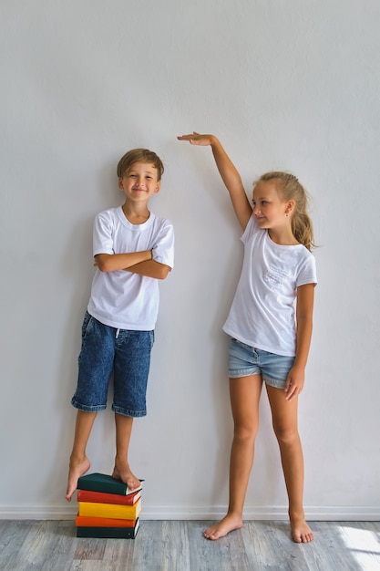 Cool kids, little boy and girl measure their height and compare, have fun near white wall