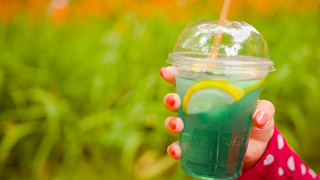 Cool lemonade in transparent cup with straw in hands of anonymous woman Unrecognizable person holding soft drink in city park