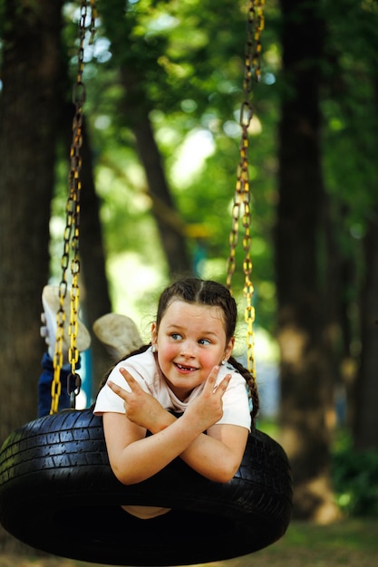 Cool little girl swinging on rubber wheel in playground in green park closeup Summer holidays in camp tourist center Walking and playing outdoors sport activity and healthy lifestyle recreation