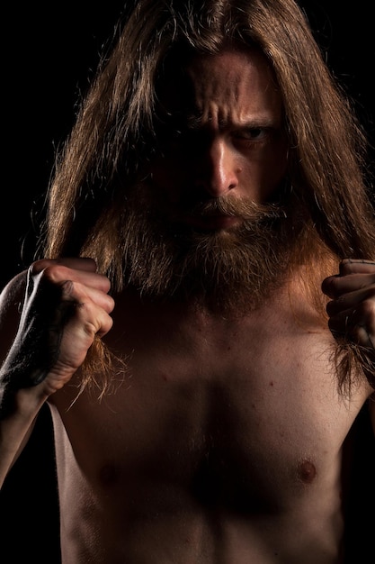 Cool looking hipster with long hair and beard on black background in studio photo. Expression and fashion