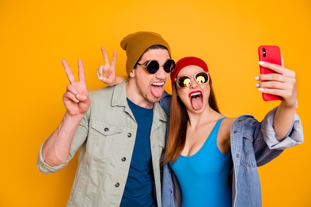 Cool modern two people students use smartphone make selfie v-sign show tongue-out summer rest blogging wear cap shirt blue swimwear denim jeans jacket isolated bright shine color background