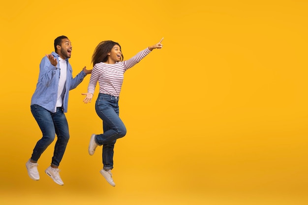 Cool offer excited joyful black couple jumping and pointing at copy space