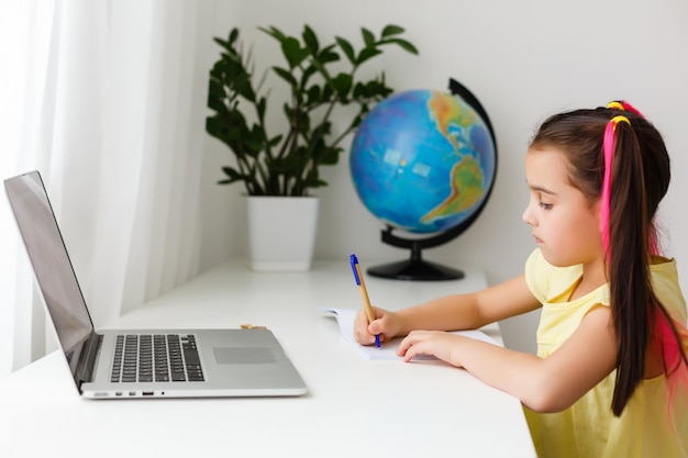 멋진 온라인 학교. 노트북을 사용하여 집에서 온라인으로 공부하는 아이. 온라인 e-러닝 시스템을 통해 공부하는 노트북 컴퓨터를 사용하는 쾌활한 어린 소녀. 원격 또는 원격 학습