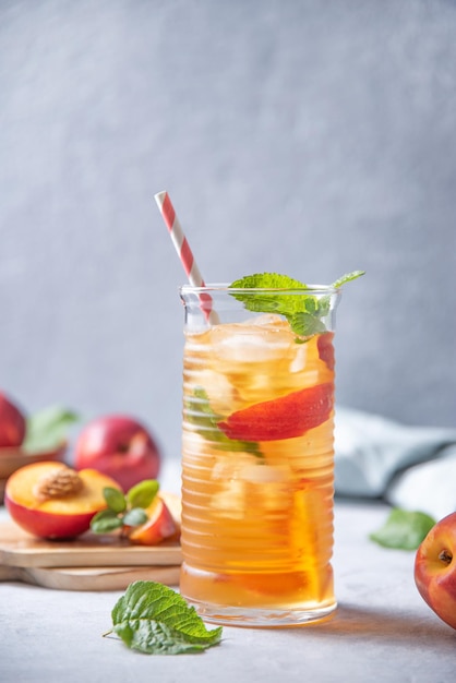 Cool peach tea with mint and ice in a glass on a blue background Vertical orientation Front view and copy space image