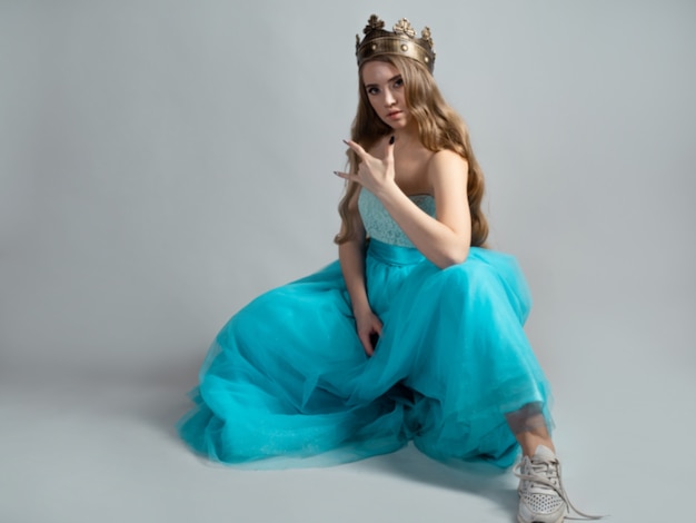 Cool princess in a lush blue dress and crown makes a rocker\
hand gesture
