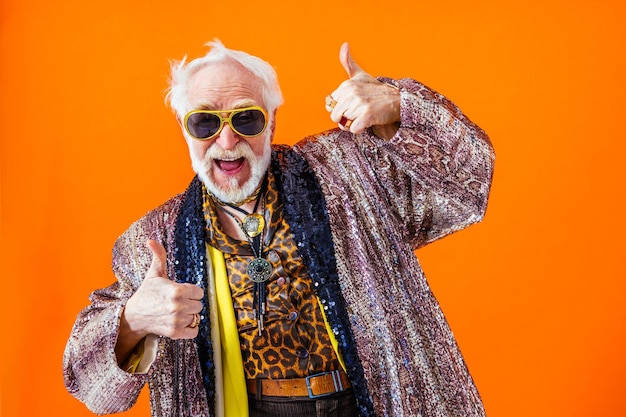 Cool senior man met modieuze kledingstijl portret op gekleurde achtergrond Grappige oude mannelijke gepensioneerde met excentrieke stijl plezier