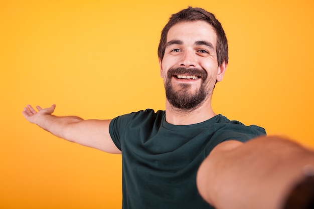 Cool smiling handsome guy smiling at the camera while taking a selfie on yellow background in studio. Recreation and lifestyle