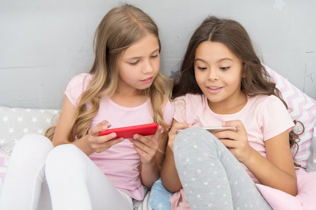 Cool sms. Small girls read sms in bed. Texting sms using smartphone. Sms message. Short message service. Text messaging by mobile phone. Mobile lifestyle. Children and technology.