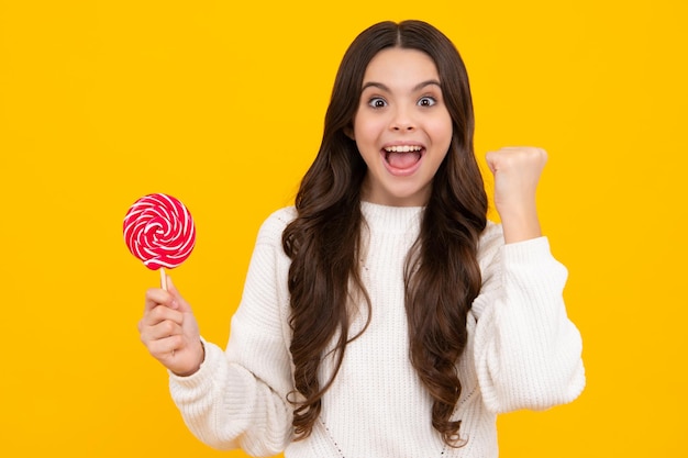 Cool teen child with lollipop over yellow isolated background Sweet childhood life Teen girl with yummy lollipop candy Excited teenager girl