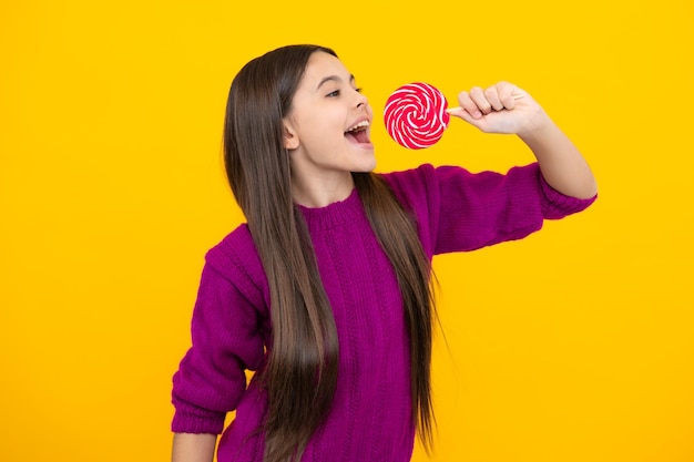 Cool teen child with lollipop over yellow isolated background Sweet childhood life Teen girl with yummy lollipop candy