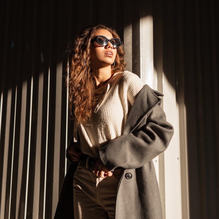 Photo cool trendy beautiful glamorous girl in autumn vogue style with a long coat and sweater with sunglasses walking on the street in sunlight