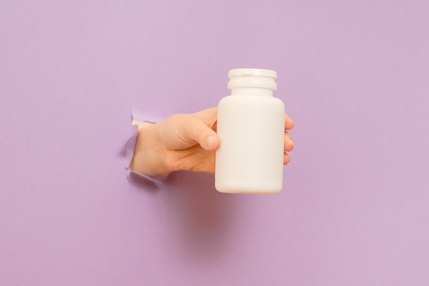 Photo cool view on white bottle plastic tube in hands on lilac background packaging for pills capsules or supplements cosmetics