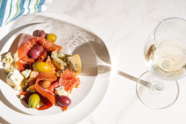 Foto vino bianco fresco in un bicchiere vicino a un piatto con prosciutto affettato, colomba, formaggio e olive varie
