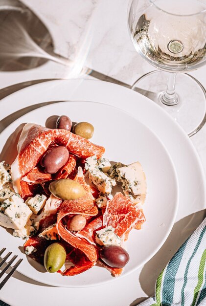 Foto vino bianco fresco in un bicchiere vicino a un piatto con fette di jamon, colomba e olive varie, uno spuntino leggero in una giornata calda, classico cibo italiano