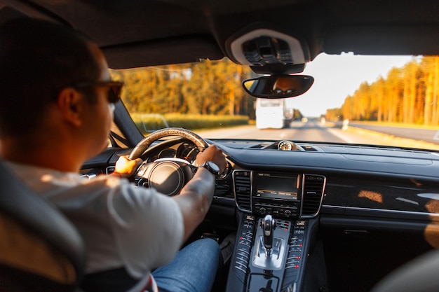 Foto cool giovane uomo d'affari con occhiali da sole guida un'auto di lusso al tramonto viaggio e viaggio in auto