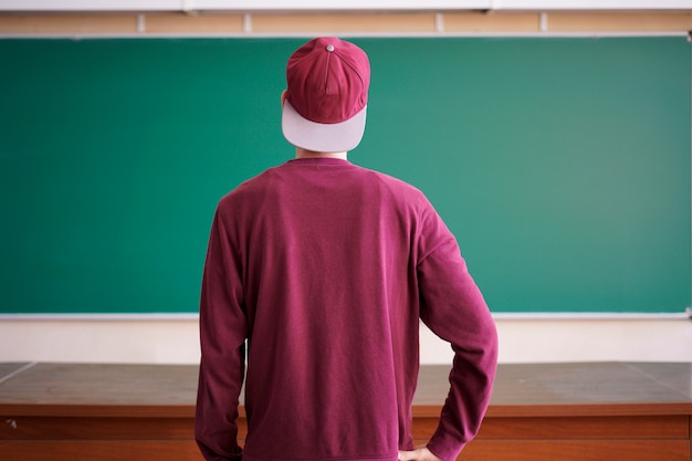 Cool young hipster student in snapback cap and casual in university with blackboard on background