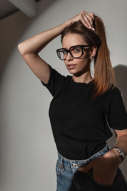 Cool young woman with stylish glasses in trendy black mockup tshirt and jeans in the studio on a white background with hard light Glamorous girl model