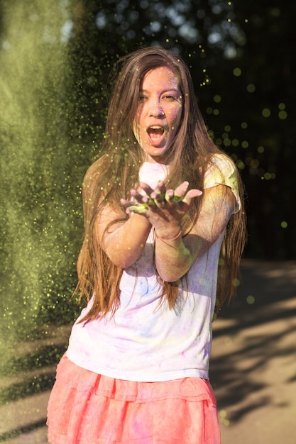 Coole brunette vrouw met wit overhemd en roze rok, spelend met kleurrijke holi-verf