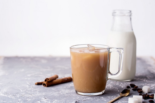 Cooled coffee with milk, cinnamon sticks, coffee beans, sugar, spoon on the table.