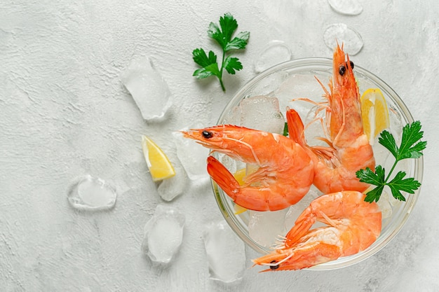 Cooled shrimps in a bowl with ice, lemon and parsley on grey background. Italian food, copy space.