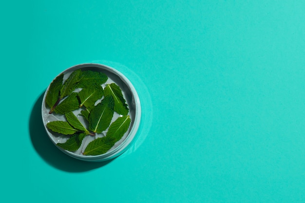 Cooling body and massage cream decorated with fresh mint leaves on a turquoise background