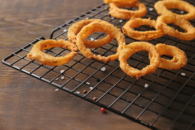 Cooling rack with fried breaded onion rings on wooden background