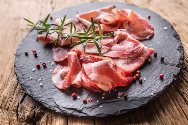 Coppa di Parma ham op leisteen bord met rozemarijn zout en peper.