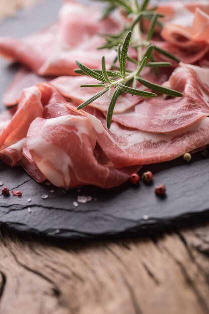 Coppa di Parma ham on slate board with rosemary salt and pepper.