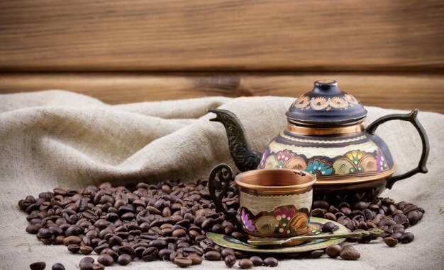 Copper cup and teapot with heap of coffee beans