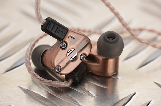 Copper metallic hybrid dynamic driver balanced armature earbuds on the aluminum metal plate.