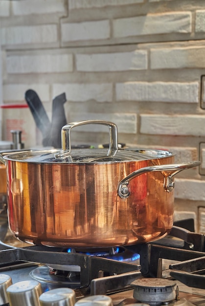 Copper saucepan with lid with dish is cooked over fire on gas stove Steam rises above the pot