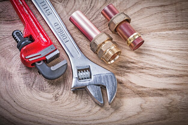 Copper water pipe wrench nipple hose connectors adjustable key on wooden board plumbing concept.