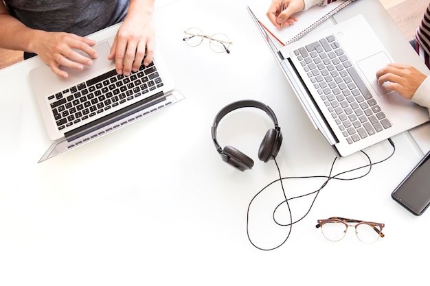 Photo copy space background of a white desk seen from above with two people working on the computer. desk with headphones, computers, mobile phone and glasses