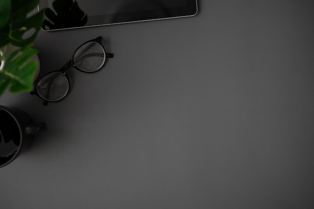 Photo a copy space on a dark grey background with eyeglasses a coffee mug a tablet and a potted plant