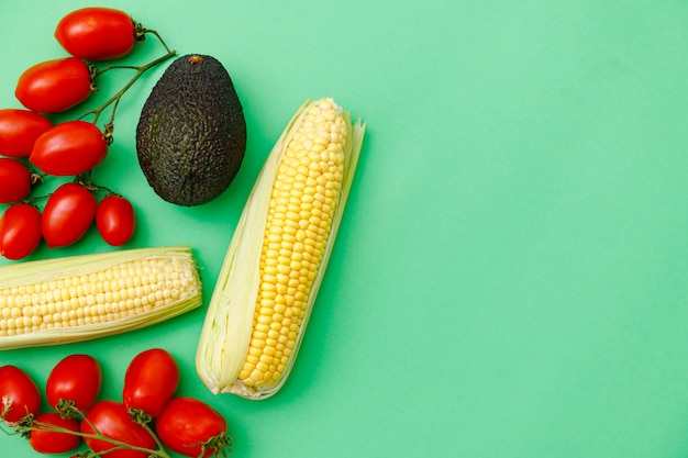 Photo copy space and fresh sweetcorn, tomatoes and avocado on green background.