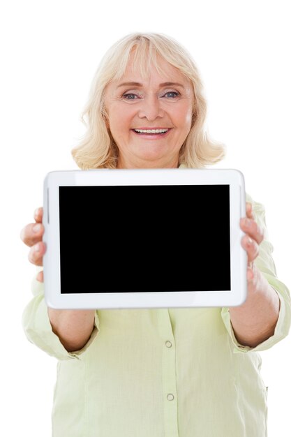 Copy space on her digital tablet. Happy senior woman showing her digital tablet and smiling while standing isolated on white background