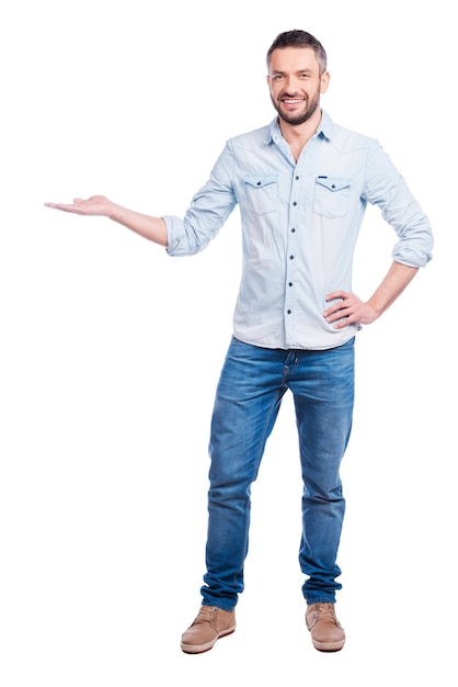 Copy space on his hand. Full length of handsome young man in casual wear holding copy space and smiling while standing isolated on white background