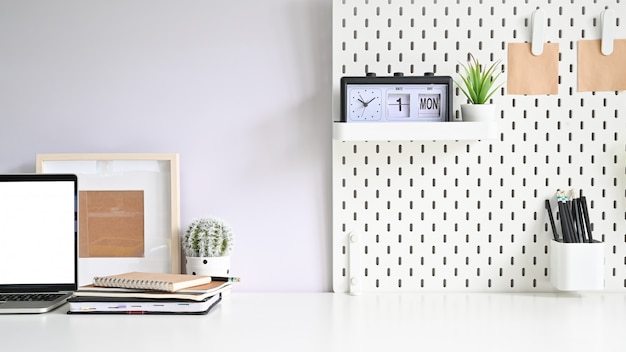 Copy space mockup laptop, pegboard, photo frame and office supply on white table 